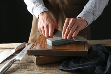 Photo of Man sharpening knife with sharpener on wooden table, closeup