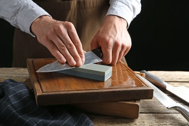 Photo of Man sharpening knife with sharpener on wooden table, closeup