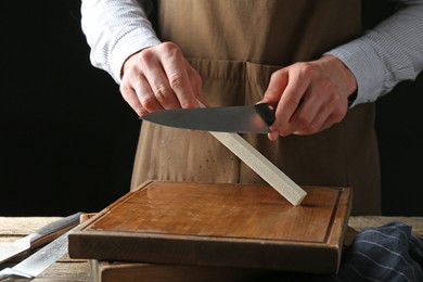 Photo of Man sharpening knife with sharpener on wooden table, closeup