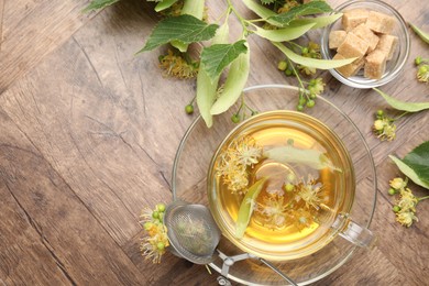 Photo of Fresh linden tea in cup, sugar cubes and flowers on wooden table, flat lay. Space for text