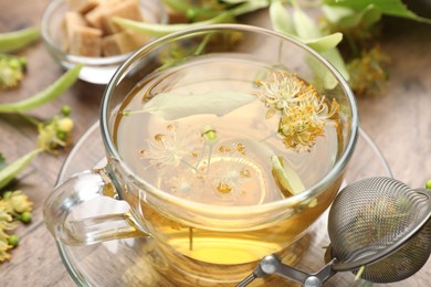 Photo of Fresh linden tea in cup, sugar cubes and flowers on wooden table, closeup