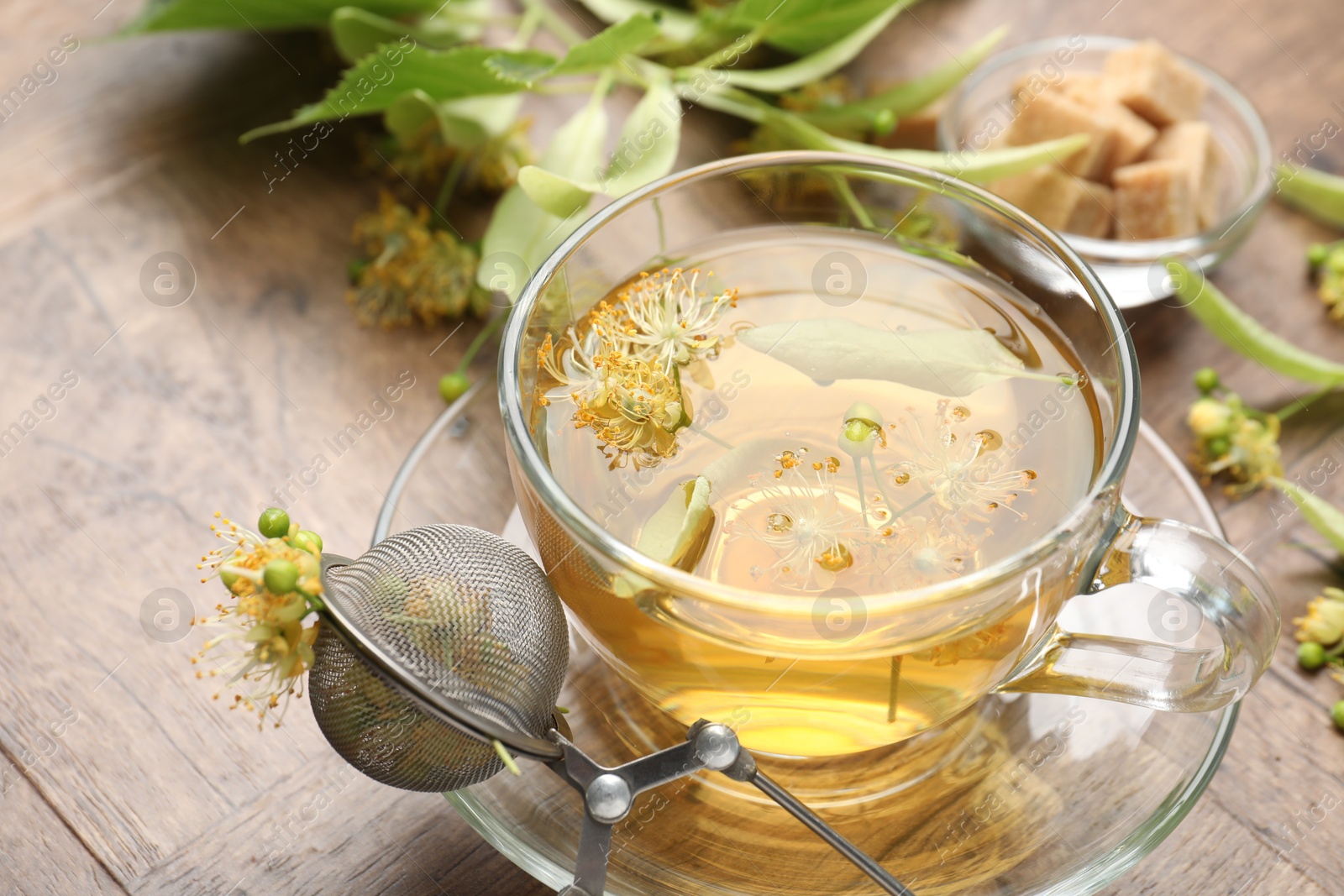 Fresh linden tea in cup, sugar cubes and flowers on wooden table, closeup Photo of Fresh linden tea in cup, sugar cubes and flowers on wooden table, closeup