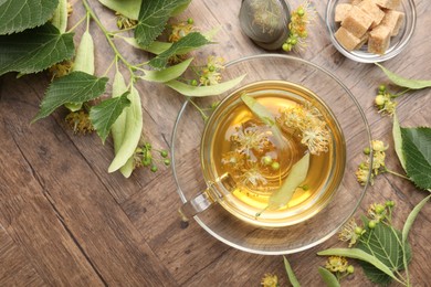 Photo of Fresh linden tea in cup, sugar cubes and flowers on wooden table, flat lay. Space for text