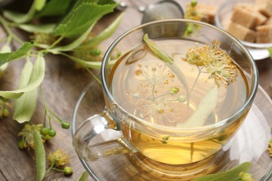 Photo of Fresh linden tea in cup, sugar cubes and flowers on wooden table, closeup