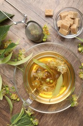 Photo of Fresh linden tea in cup, sugar cubes and flowers on wooden table, flat lay