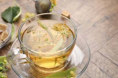 Photo of Fresh linden tea in cup, sugar cubes and flowers on wooden table, closeup. Space for text