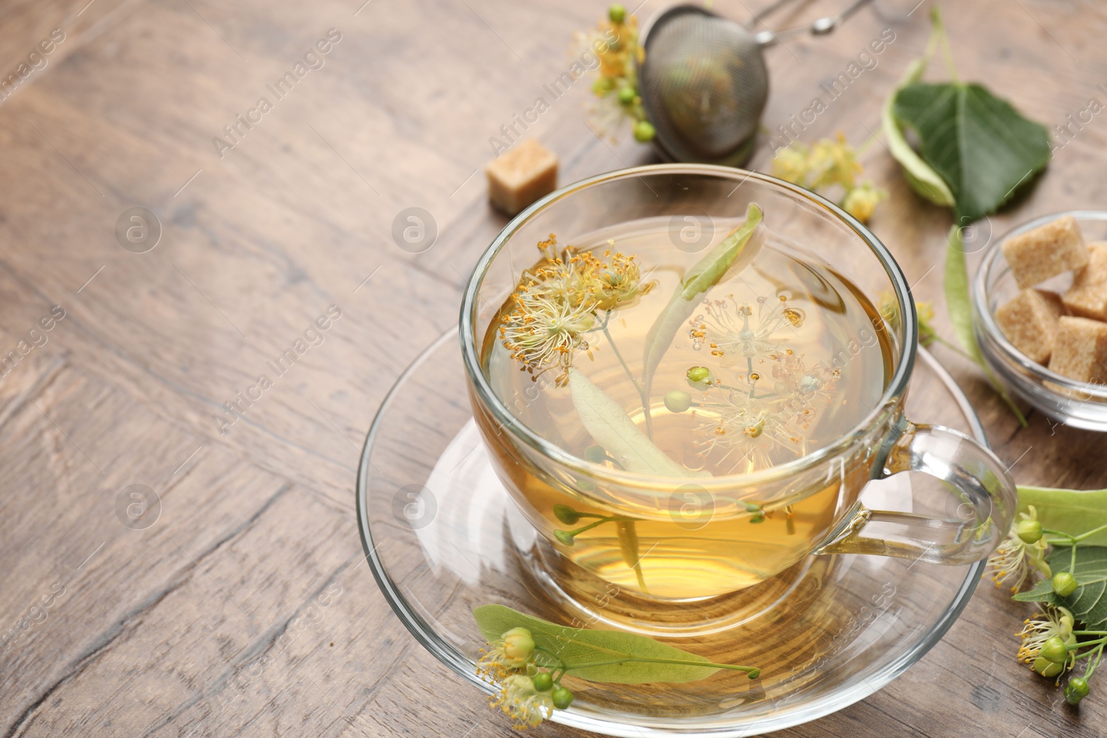 Fresh linden tea in cup, sugar cubes and flowers on wooden table, closeup. Space for text Photo of Fresh linden tea in cup, sugar cubes and flowers on wooden table, closeup. Space for text