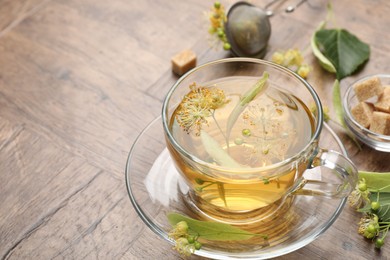 Photo of Fresh linden tea in cup, sugar cubes and flowers on wooden table, closeup. Space for text