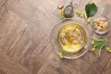Photo of Fresh linden tea in cup, sugar cubes and flowers on wooden table, flat lay. Space for text