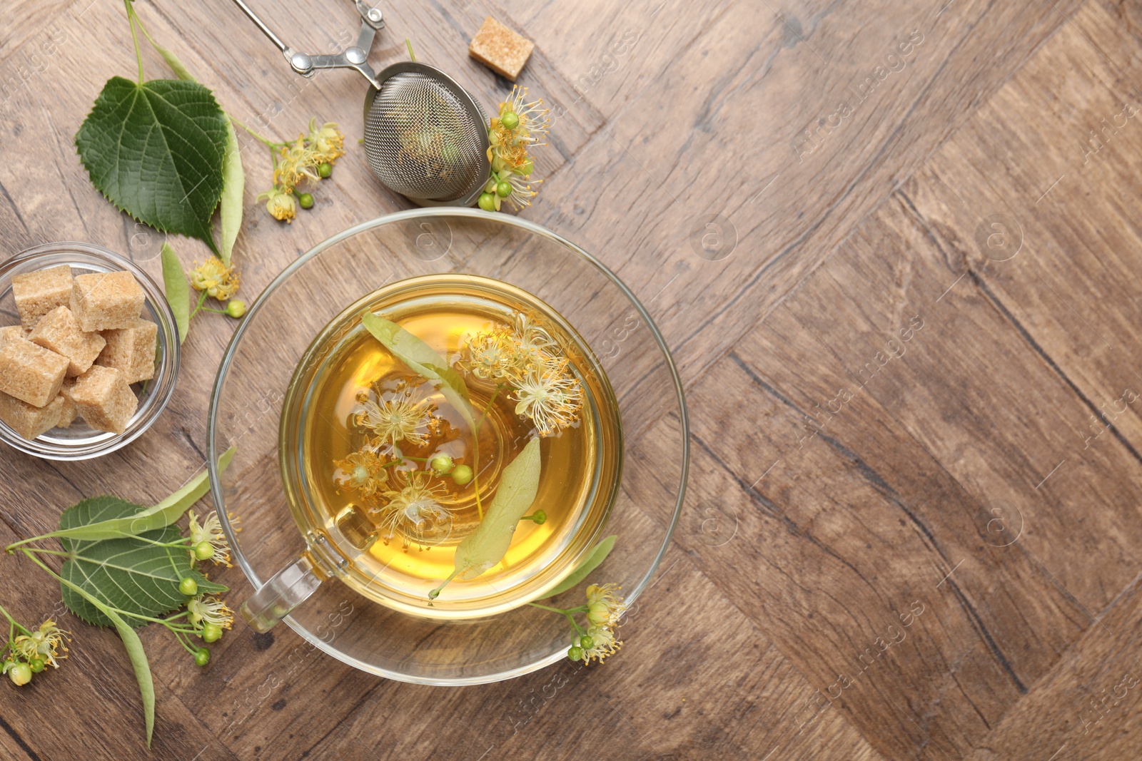 Fresh linden tea in cup, sugar cubes and flowers on wooden table, flat lay. Space for text Photo of Fresh linden tea in cup, sugar cubes and flowers on wooden table, flat lay. Space for text