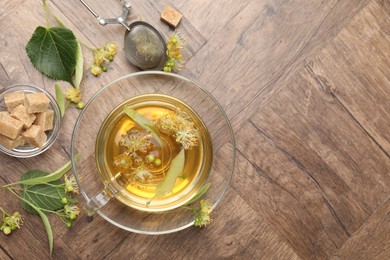 Photo of Fresh linden tea in cup, sugar cubes and flowers on wooden table, flat lay. Space for text