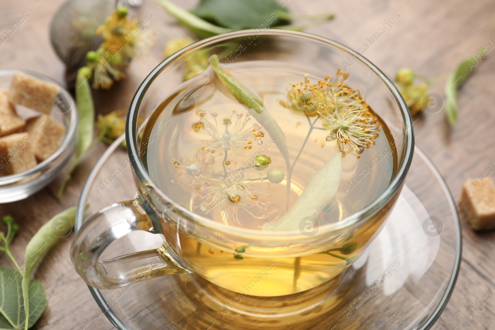 Fresh linden tea in cup, sugar cubes and flowers on wooden table, closeup Photo of Fresh linden tea in cup, sugar cubes and flowers on wooden table, closeup