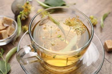 Photo of Fresh linden tea in cup, sugar cubes and flowers on wooden table, closeup