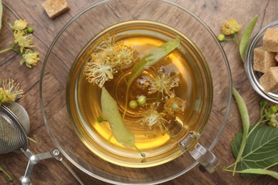 Photo of Fresh linden tea in cup, sugar cubes and flowers on wooden table, flat lay