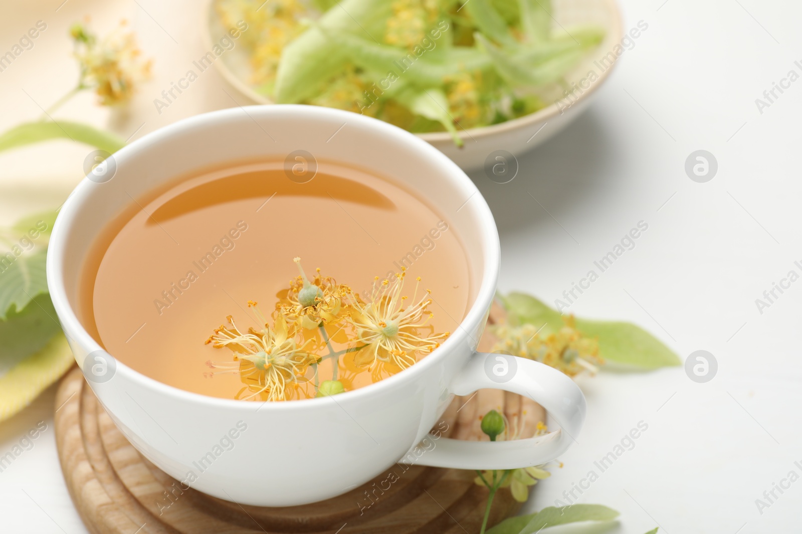 Fresh linden tea in cup and flowers on white table, closeup Photo of Fresh linden tea in cup and flowers on white table, closeup