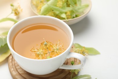 Photo of Fresh linden tea in cup and flowers on white table, closeup