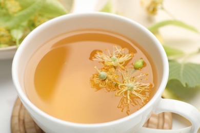 Photo of Fresh linden tea in cup and flowers on white table, closeup