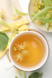 Photo of Fresh linden tea in cup and flowers on white wooden table, flat lay