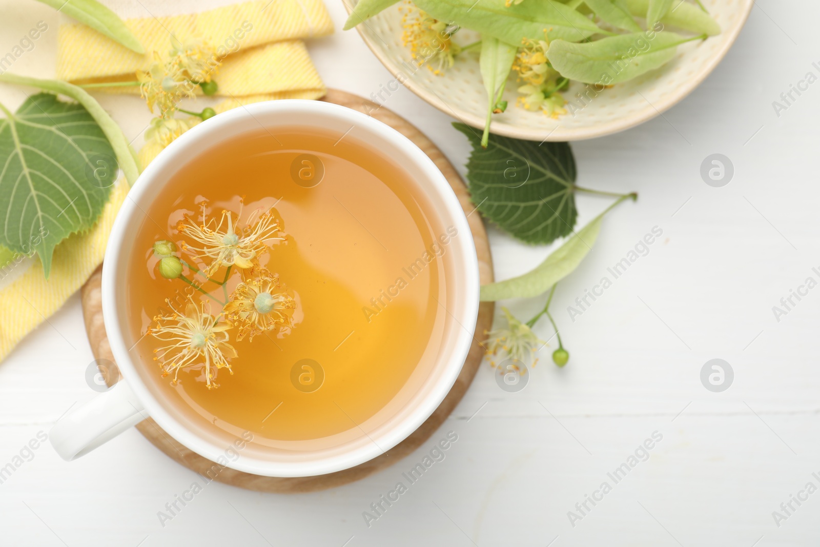 Fresh linden tea in cup and flowers on white wooden table, flat lay. Space for text Photo of Fresh linden tea in cup and flowers on white wooden table, flat lay. Space for text