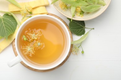 Photo of Fresh linden tea in cup and flowers on white wooden table, flat lay. Space for text