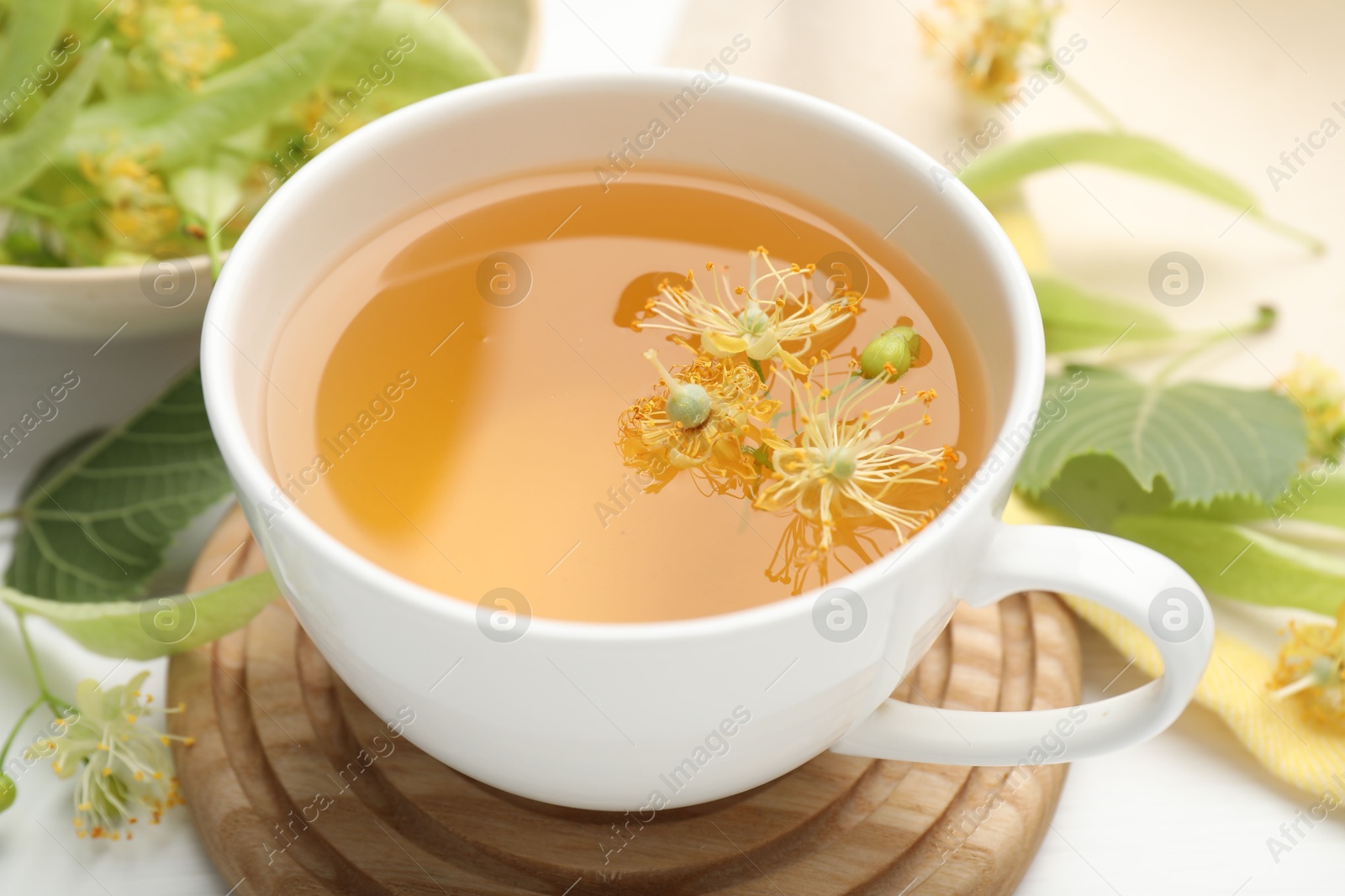 Fresh linden tea in cup and flowers on white table, closeup Photo of Fresh linden tea in cup and flowers on white table, closeup