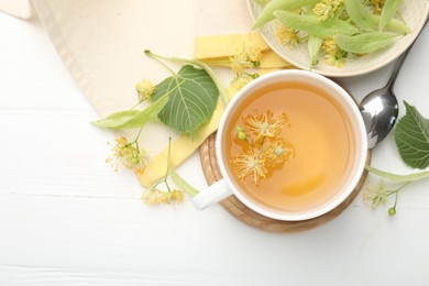 Photo of Fresh linden tea in cup and flowers on white wooden table, flat lay. Space for text