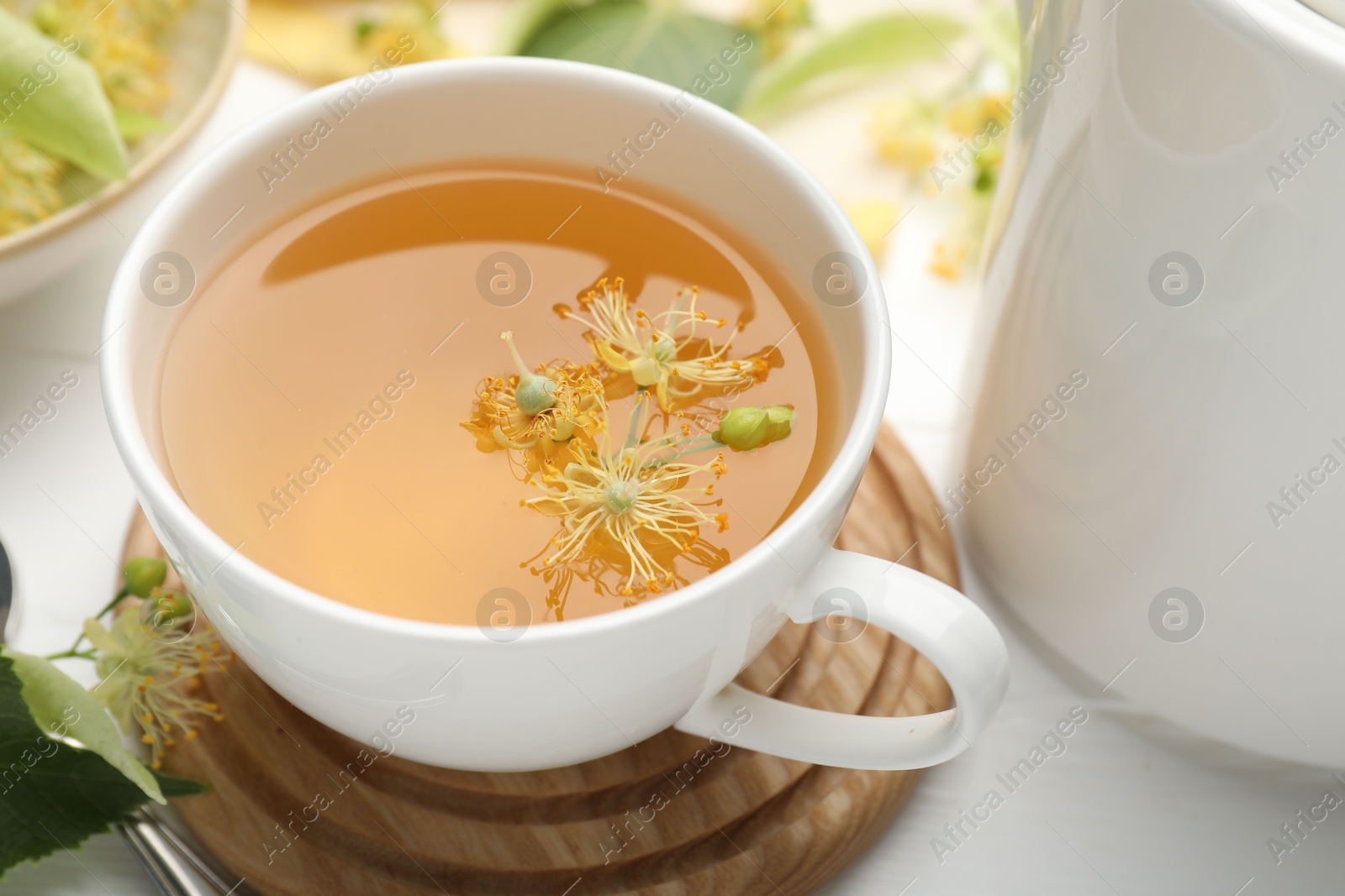Fresh linden tea in cup and flowers on white wooden table, closeup Photo of Fresh linden tea in cup and flowers on white wooden table, closeup