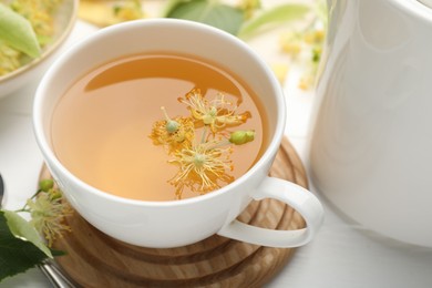 Photo of Fresh linden tea in cup and flowers on white wooden table, closeup