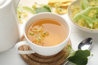 Photo of Fresh linden tea in cup and flowers on white wooden table, closeup
