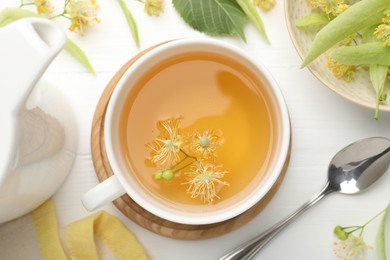 Photo of Fresh linden tea in cup and flowers on white wooden table, flat lay