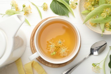 Photo of Fresh linden tea in cup and flowers on white wooden table, flat lay