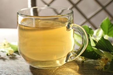 Photo of Fresh linden tea in cup and flowers on wooden table, closeup
