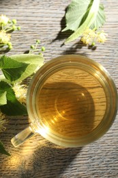 Photo of Fresh linden tea in cup and flowers on wooden table, flat lay