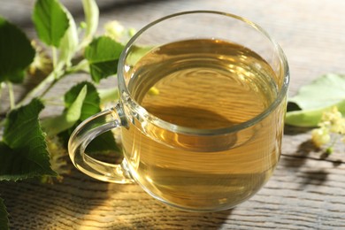 Photo of Fresh linden tea in cup and flowers on wooden table, closeup