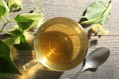 Photo of Fresh linden tea in cup and flowers on wooden table, flat lay