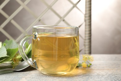 Photo of Fresh linden tea in cup and flowers on wooden table, closeup