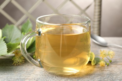 Photo of Fresh linden tea in cup and flowers on wooden table, closeup