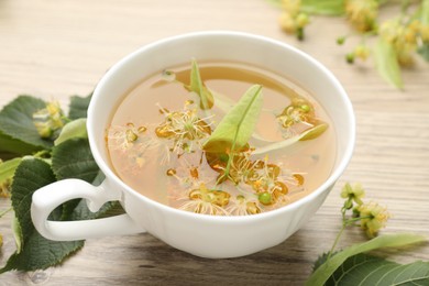 Photo of Fresh linden tea in cup and flowers on wooden table, closeup
