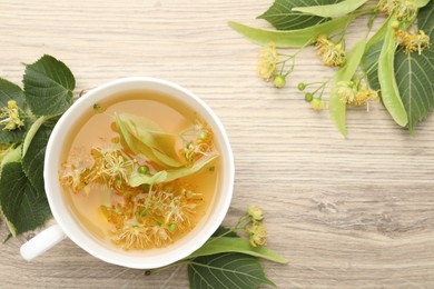 Photo of Fresh linden tea in cup and flowers on wooden table, flat lay. Space for text