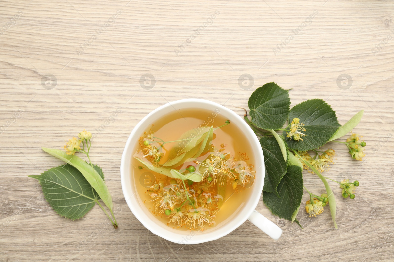 Fresh linden tea in cup and flowers on wooden table, flat lay. Space for text Photo of Fresh linden tea in cup and flowers on wooden table, flat lay. Space for text