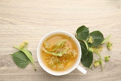 Photo of Fresh linden tea in cup and flowers on wooden table, flat lay. Space for text