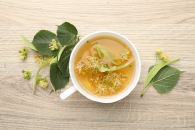 Photo of Fresh linden tea in cup and flowers on wooden table, flat lay