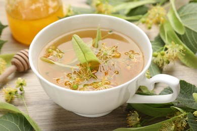 Photo of Fresh linden tea in cup, honey and flowers on wooden table, closeup