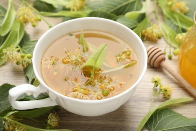 Photo of Fresh linden tea in cup, honey and flowers on wooden table, closeup