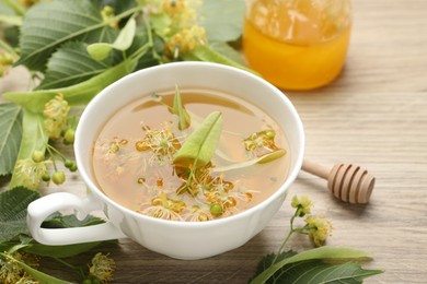 Photo of Fresh linden tea in cup, honey and flowers on wooden table, closeup