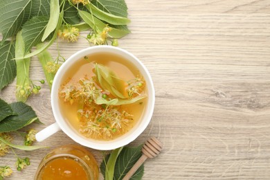 Photo of Fresh linden tea in cup, honey and flowers on wooden table, flat lay. Space for text