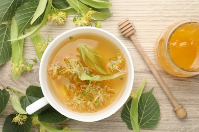 Photo of Fresh linden tea in cup, honey and flowers on wooden table, flat lay