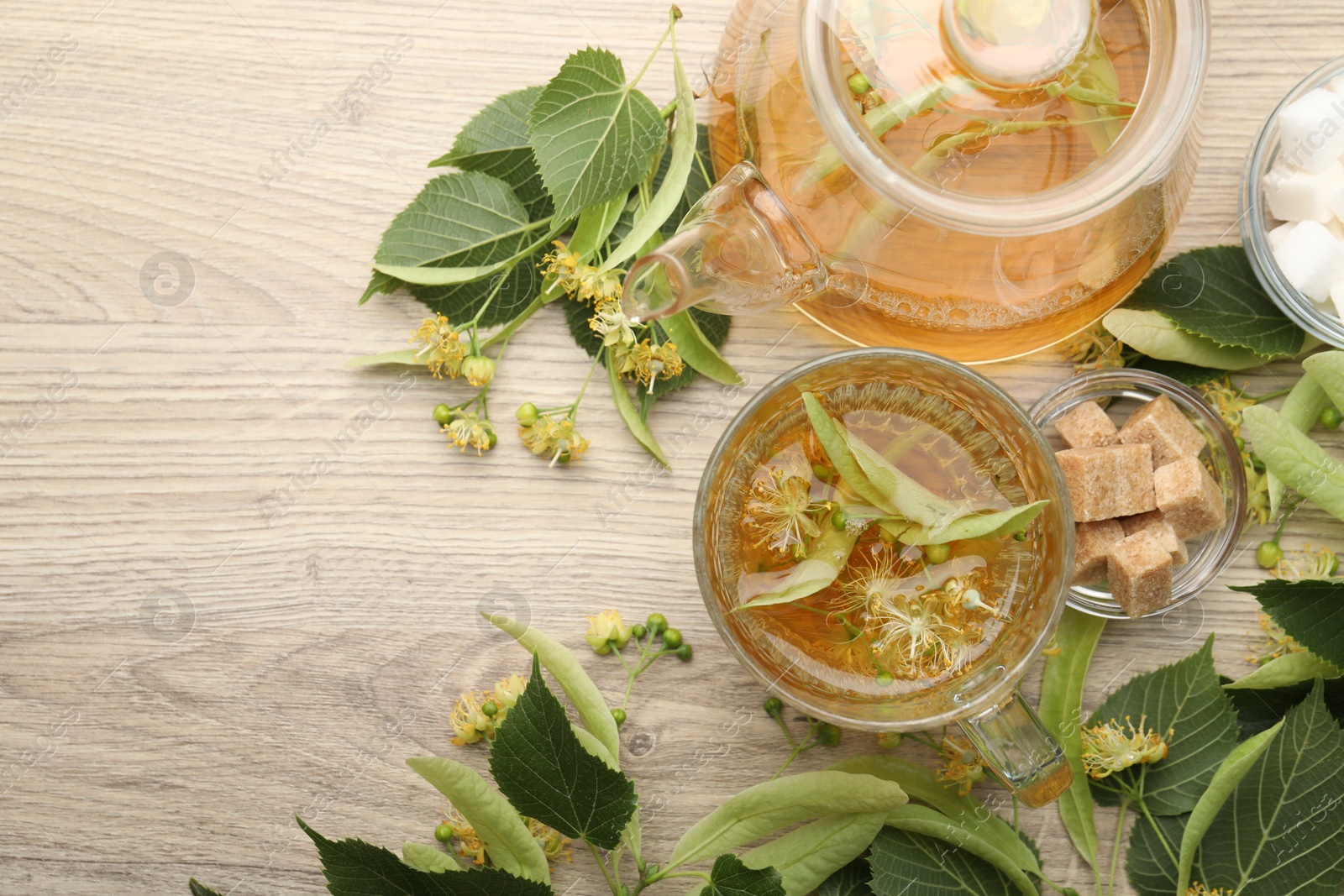 Fresh linden tea in cup, teapot, sugar cubes and flowers on wooden table, flat lay. Space for text Photo of Fresh linden tea in cup, teapot, sugar cubes and flowers on wooden table, flat lay. Space for text