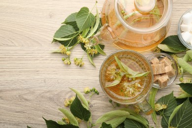 Photo of Fresh linden tea in cup, teapot, sugar cubes and flowers on wooden table, flat lay. Space for text