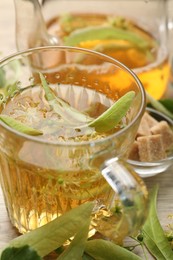 Photo of Fresh linden tea in cup, teapot, sugar cubes and flowers on wooden table, closeup